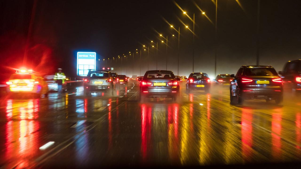A busy British motorway at night in the rain with a Police car on the hard shoulder