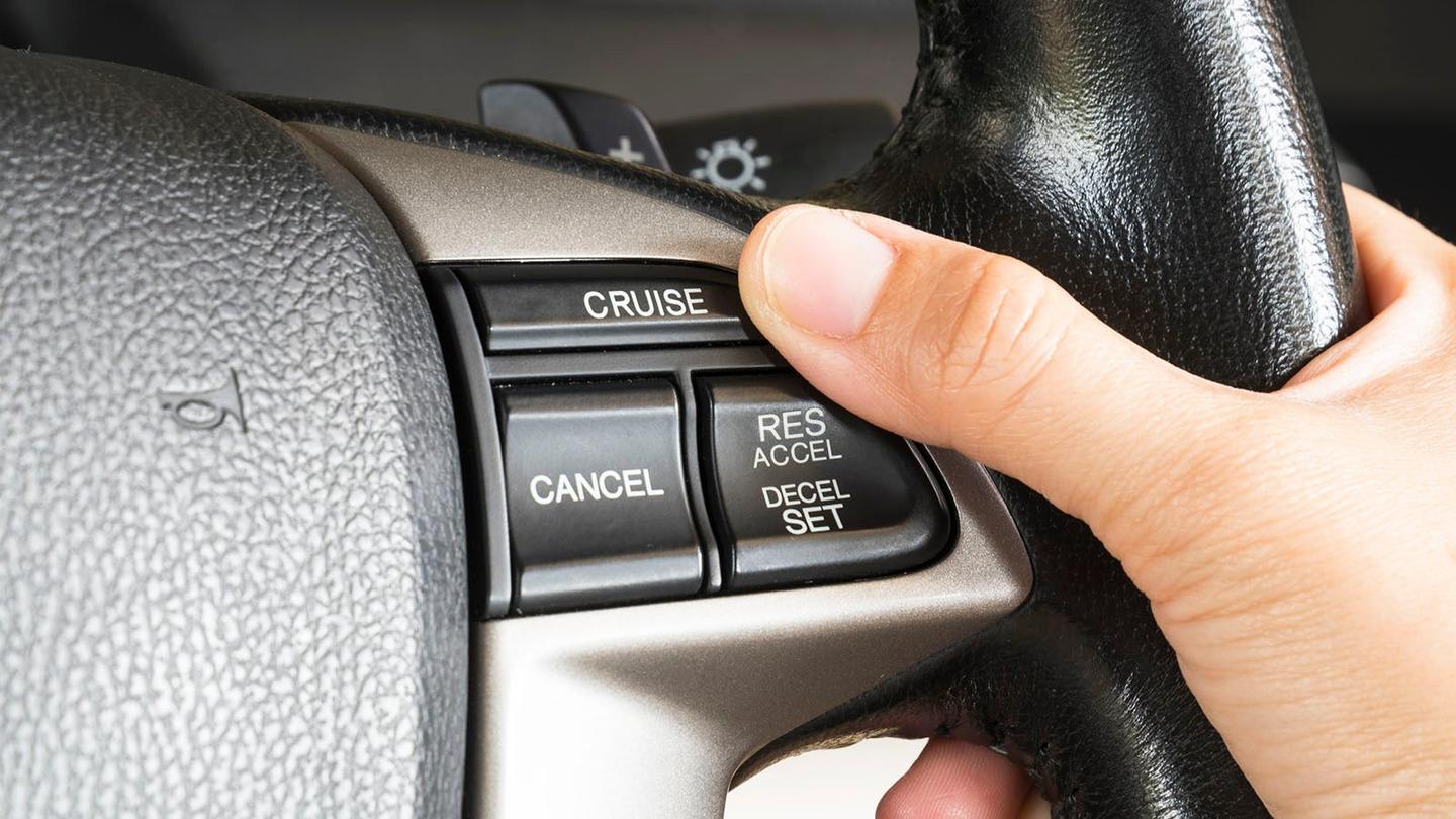 driver pressing cruise control button on steering wheel