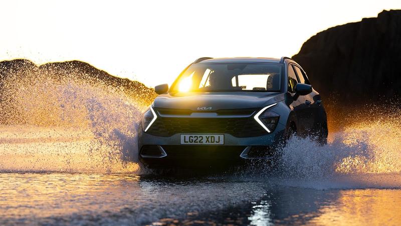 Kia Sportage in grey dramatically splashing through a shallow stream with the sunset gracefully glinting through the car's windows