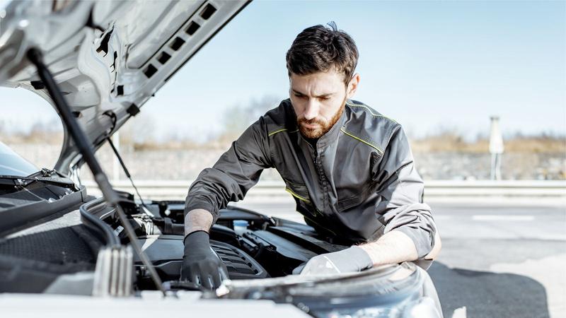A mechanic in grey overalls works under the bonnet of a van