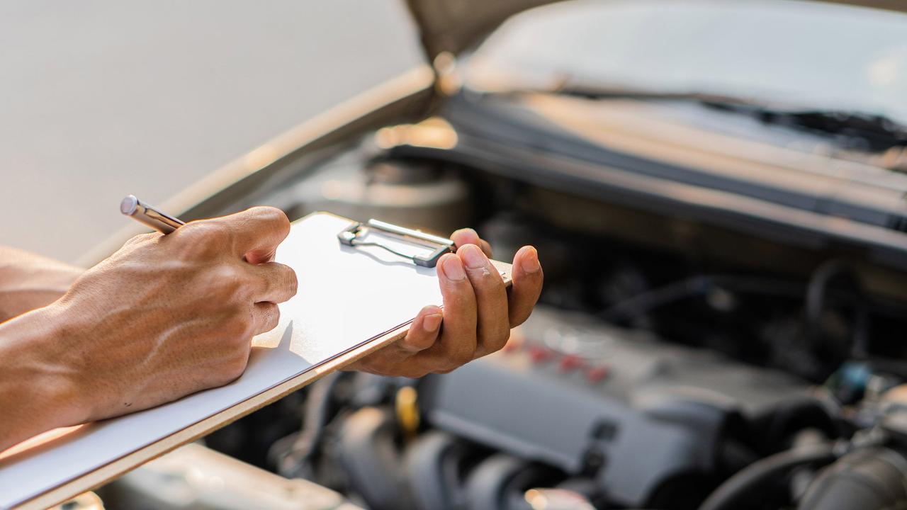 Person with clipboard in front of car engine bay