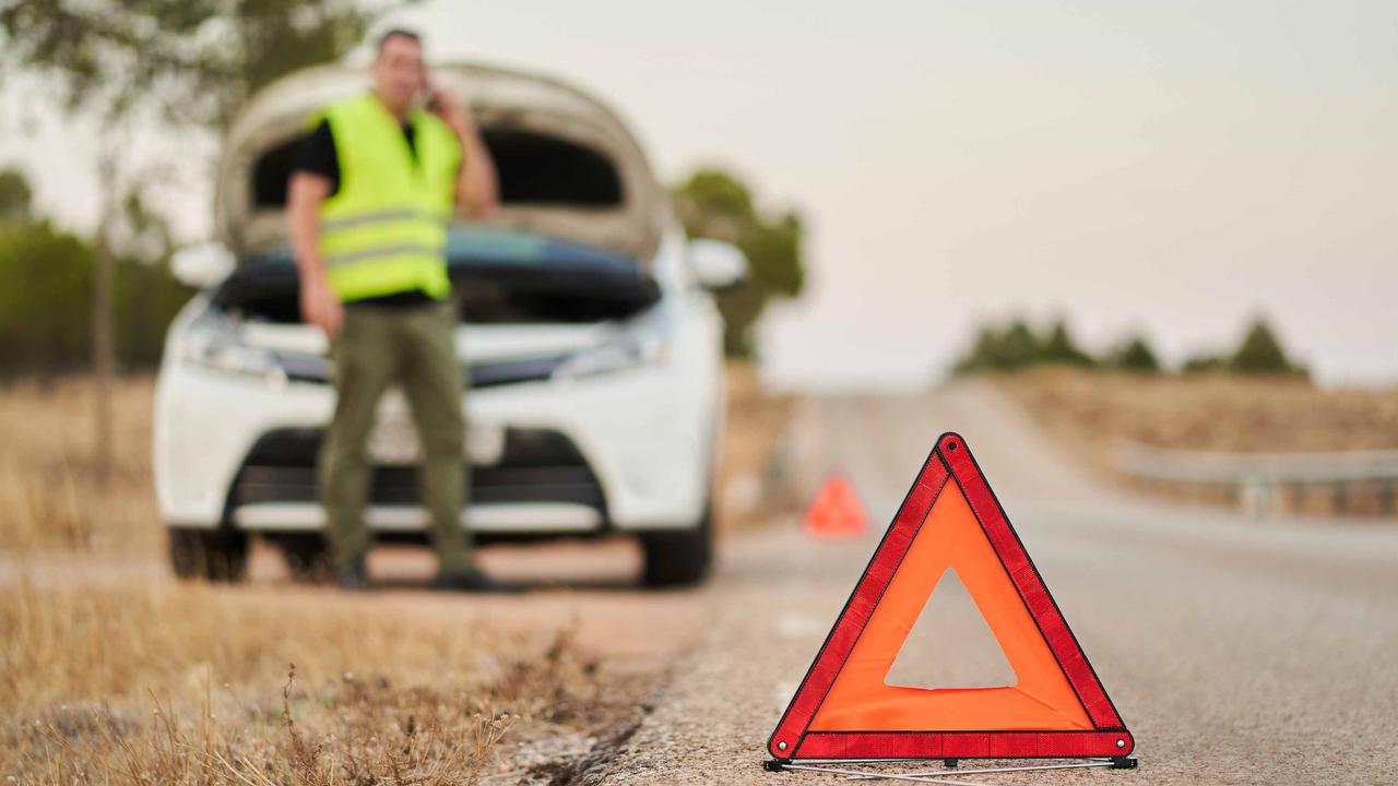 Man in hi-vis jacket stood by broken-down car, with warning triangle in the foreground