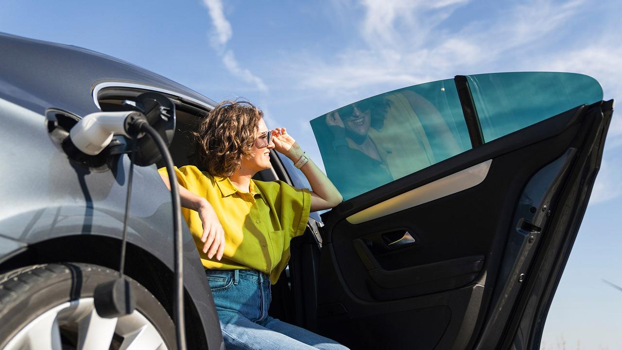 Passenger with sunglasses sits in the back of a charging EV