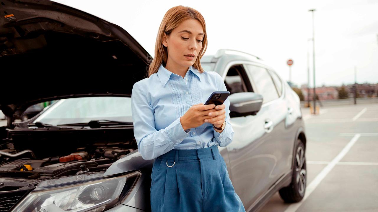Female driver on her phone next to car with bonnet up
